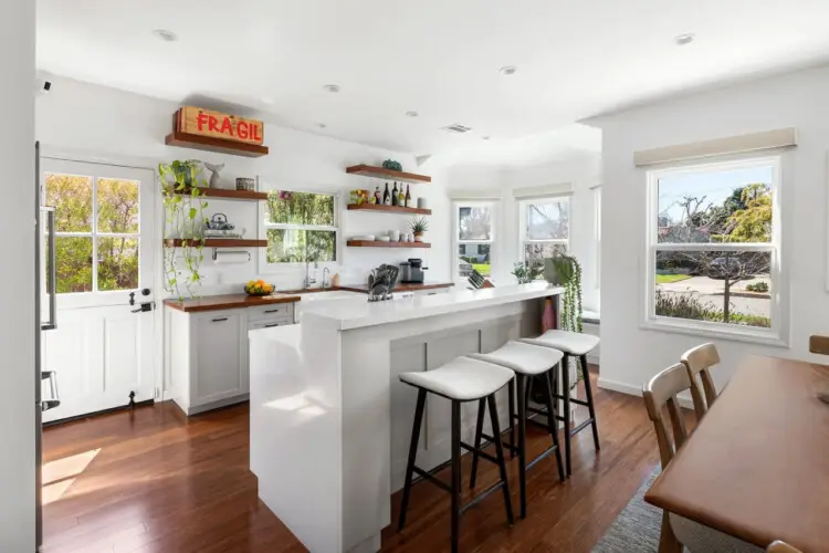 Kitchen with white island, bar stools, and open shelving at Sun-Drenched Spanish Manor in Mar Vista - by Open Air Homes.