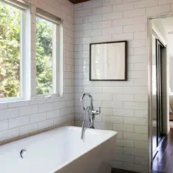 Bathroom with large bathtub, white tiles, and wooden ceiling at Sun-Drenched Spanish Manor in Mar Vista - by Open Air Homes.