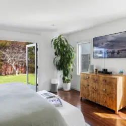 Bedroom with bed, wooden dresser, mirror, and potted plant at Sun-Drenched Spanish Manor in Mar Vista - by Open Air Homes.