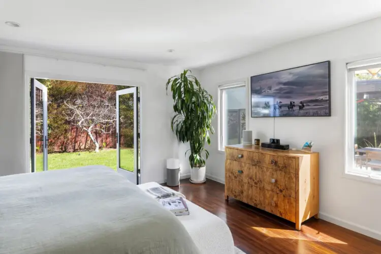 Bedroom with bed, wooden dresser, mirror, and potted plant at Sun-Drenched Spanish Manor in Mar Vista - by Open Air Homes.