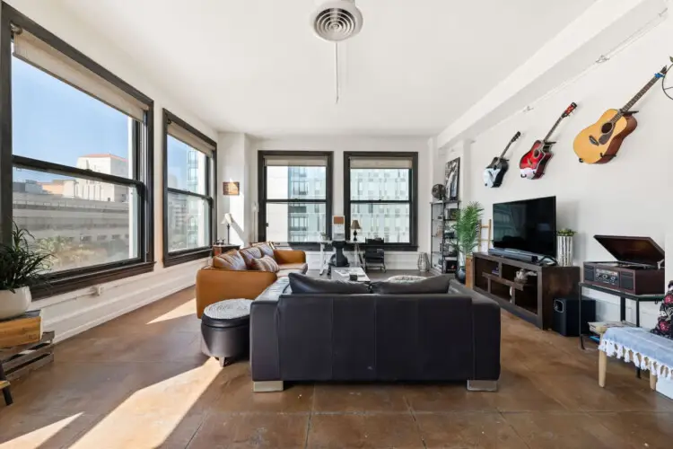 Living room with large windows, leather sofa, and TV at Skyline View Loft with Chef's Kitchen: DTLA - by Open Air Homes.