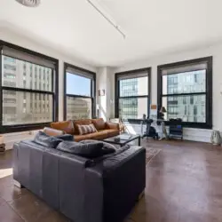 Living room with large windows, leather sofa, and TV at Skyline View Loft with Chef's Kitchen: DTLA - by Open Air Homes.