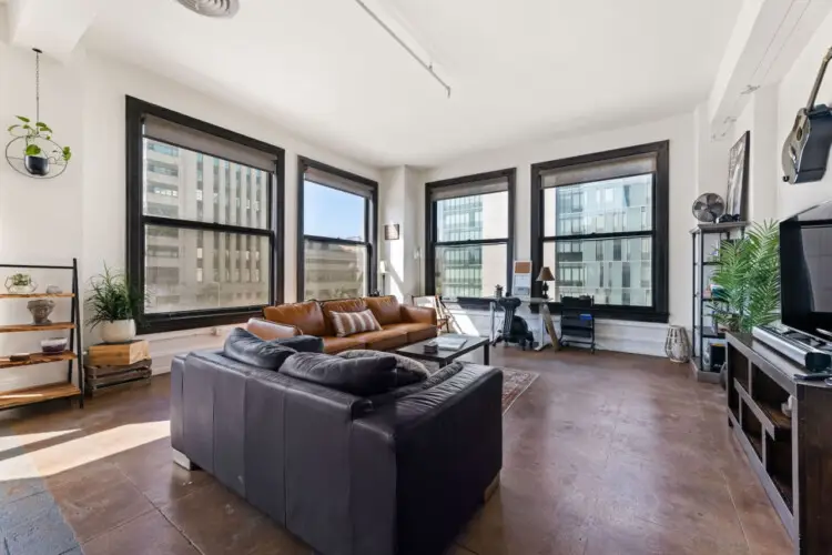 Living room with large windows, leather sofa, and TV at Skyline View Loft with Chef's Kitchen: DTLA - by Open Air Homes.