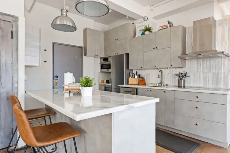 Modern kitchen with marble countertop, chairs, and stainless steel appliances at Skyline View Loft with Chef's Kitchen: DTLA - by Open Air Homes.