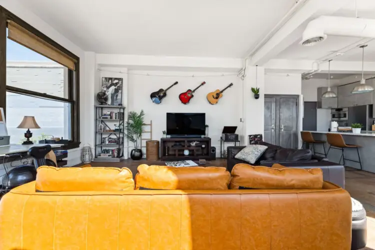 Living room with large windows, leather sofa, and TV at Skyline View Loft with Chef's Kitchen: DTLA - by Open Air Homes.