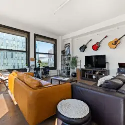 Living room with large windows, leather sofa, TV, and guitars on the wall at Skyline View Loft with Chef's Kitchen: DTLA - by Open Air Homes.