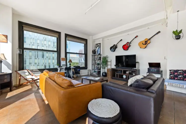 Living room with large windows, leather sofa, TV, and guitars on the wall at Skyline View Loft with Chef's Kitchen: DTLA - by Open Air Homes.