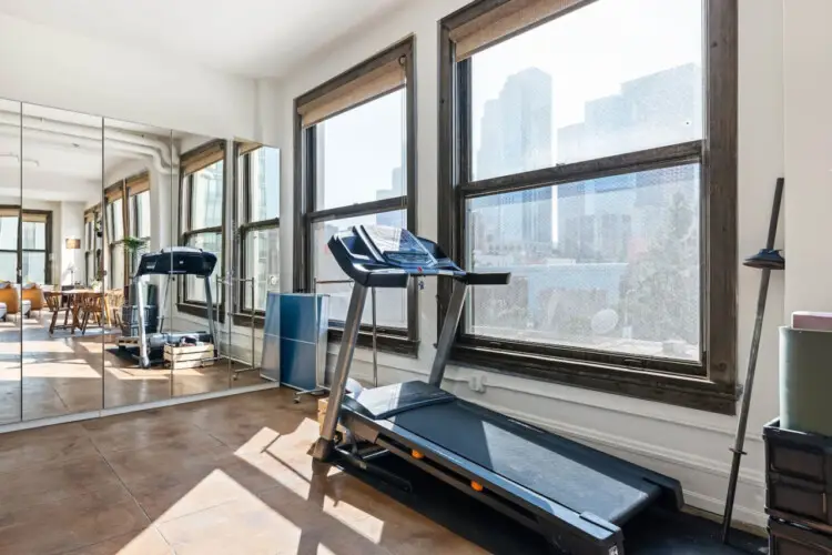 Fitness area with a treadmill and large windows offering city views at Skyline View Loft with Chef's Kitchen: DTLA - by Open Air Homes.