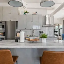 Modern kitchen with central island, pendant lighting, and bar stools at Skyline View Loft with Chef's Kitchen: DTLA - by Open Air Homes.