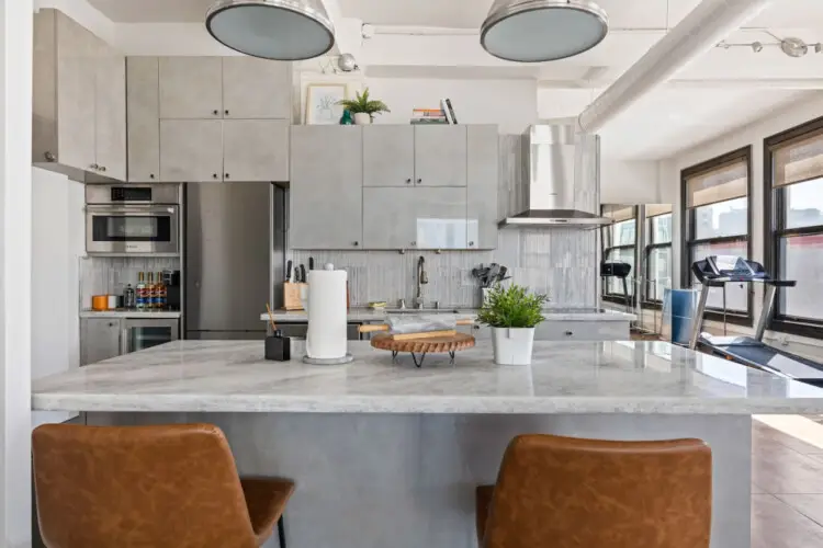 Modern kitchen with central island, pendant lighting, and bar stools at Skyline View Loft with Chef's Kitchen: DTLA - by Open Air Homes.