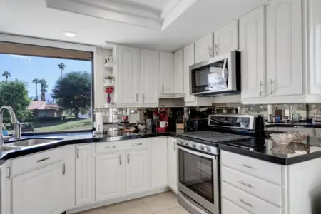 Kitchen with white cabinets, stove, and window overlooking landscaped area - by Open Air Homes