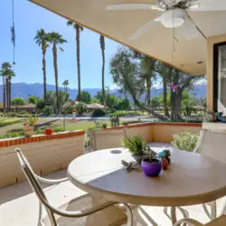 Outdoor patio area with table and chairs, overlooking landscaped area with palm trees and mountains at Sunrise Serenity: Panoramic Views & Resort Living - by Open Air Homes