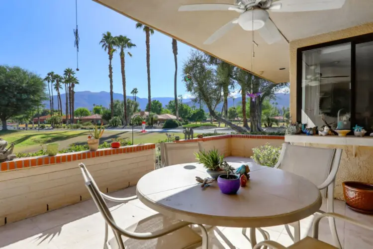 Outdoor patio area with table and chairs, overlooking landscaped area with palm trees and mountains at Sunrise Serenity: Panoramic Views & Resort Living - by Open Air Homes