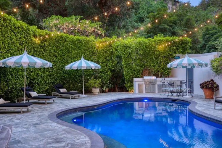 Outdoor pool area with seating, umbrellas, and barbecue setup at Laurel Canyon Classic Hollywood Residence by Open Air Homes.