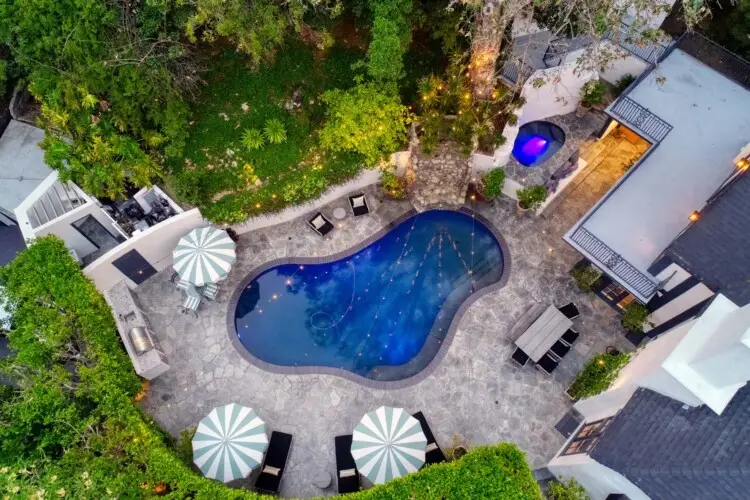 Aerial view of the outdoor pool area with seating, umbrellas, and greenery at Laurel Canyon Classic Hollywood Residence by Open Air Homes.