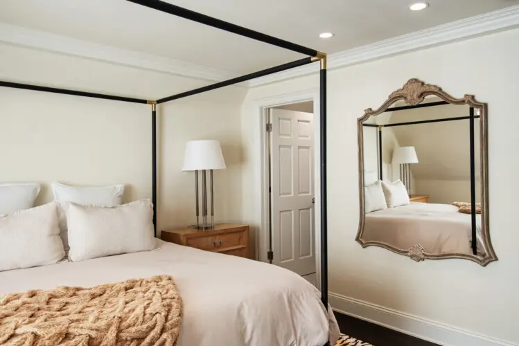 Bedroom interior of Laurel Canyon Classic Hollywood Residence W/ Pool featuring a bed with a canopy frame, bedside table with a lamp, and a large decorative mirror by Open Air Homes.