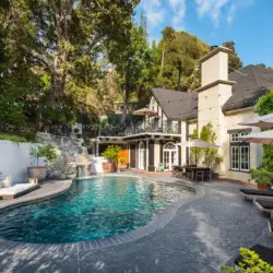 Pool area of Laurel Canyon Classic Hollywood Residence W/ Pool with stone patio, lounge chairs, umbrellas, and house in the background by Open Air Homes.