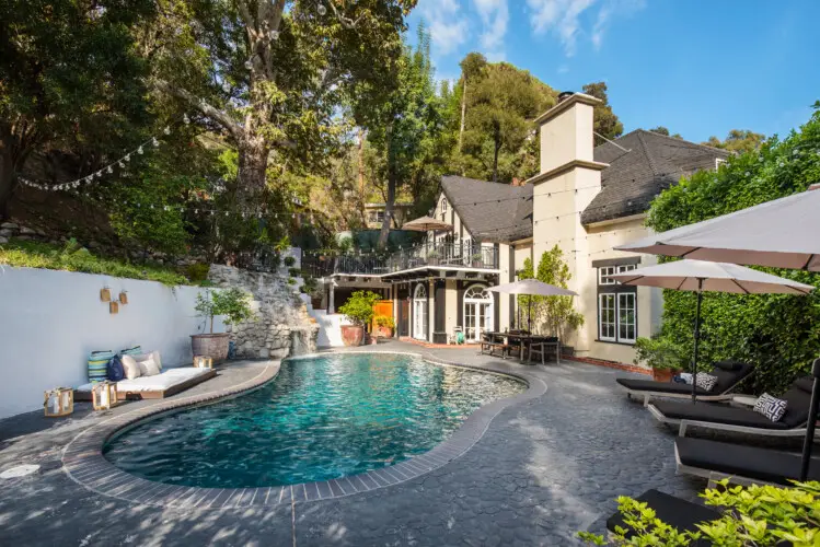 Pool area of Laurel Canyon Classic Hollywood Residence W/ Pool with stone patio, lounge chairs, umbrellas, and house in the background by Open Air Homes.