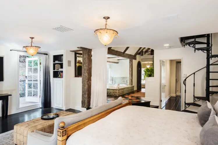 Bedroom interior of Laurel Canyon Classic Hollywood Residence W/ Pool with exposed wooden beams, bed, spiral staircase, and balcony by Open Air Homes.