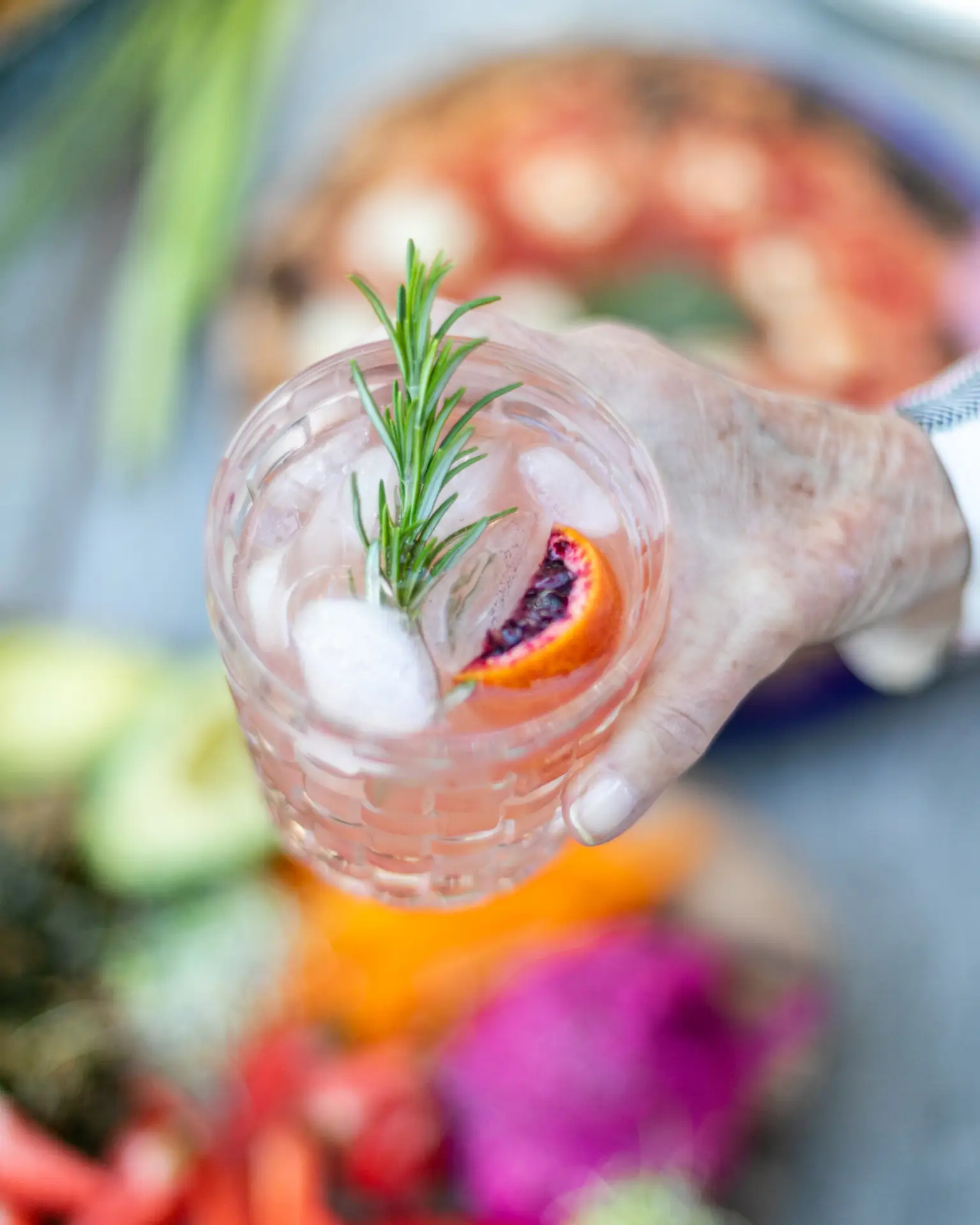 Person holding a beverage with orange slice and rosemary at Open Air Homes vacation rental