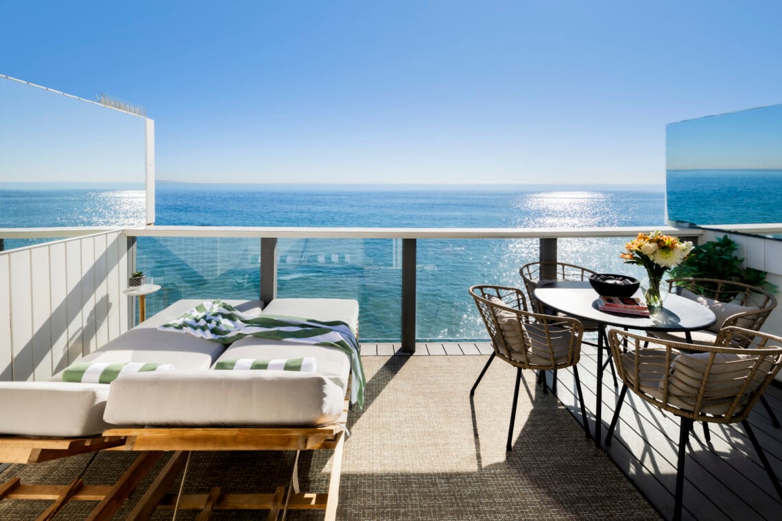 Outdoor deck with sun loungers and dining table overlooking the ocean – Open Air Homes