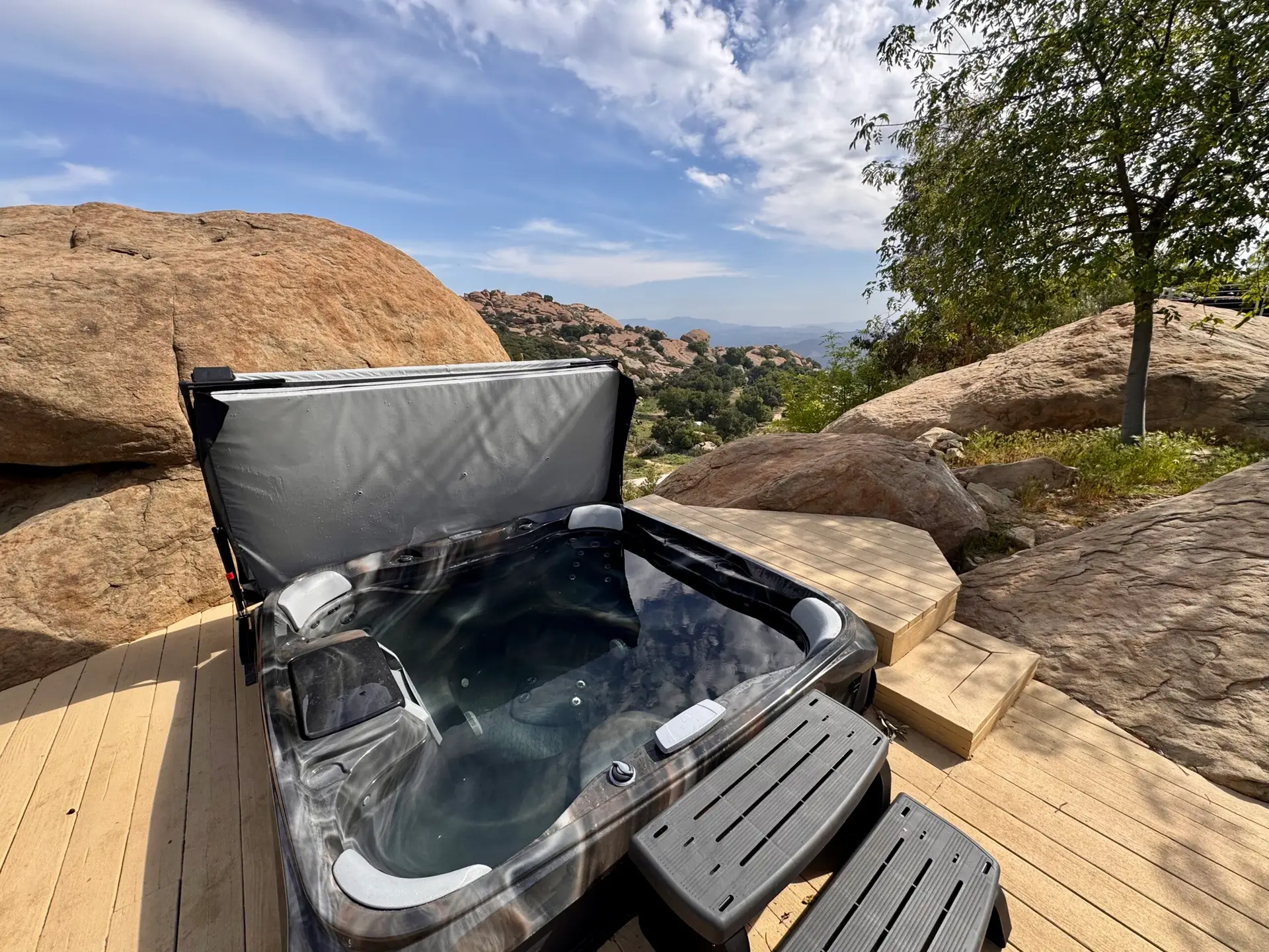 Outdoor hot tub on a wooden deck with a scenic rocky landscape view – Open Air Homes