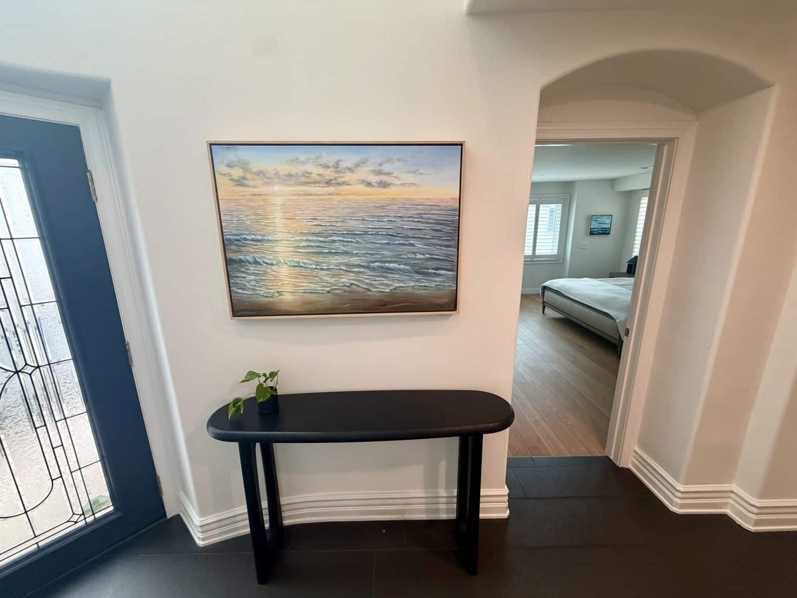 Entry console with a sunrise seascape above it, looking through an arch into a king bedroom at the Rosecrans home in Manhattan Beach