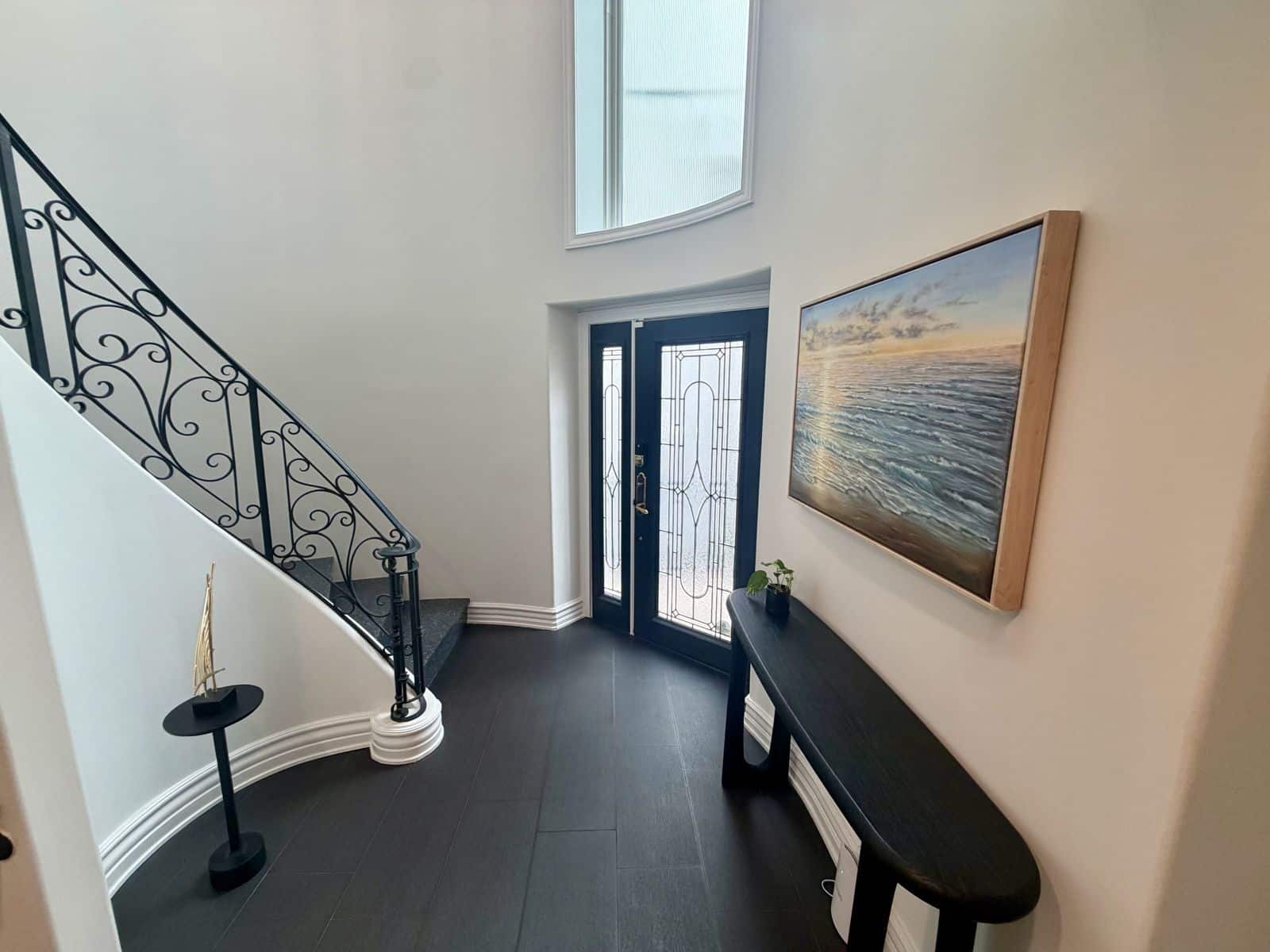 Double height entry with a curved stone staircase, black iron railing and a framed seascape at the Rosecrans home in Manhattan Beach