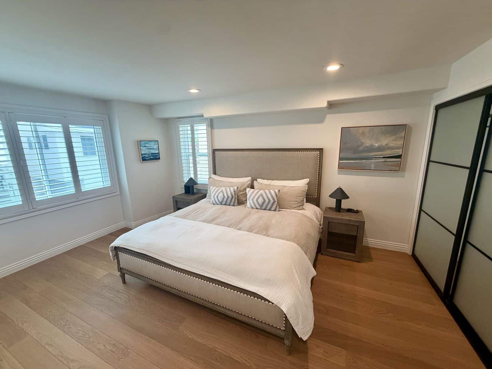 Primary bedroom with an upholstered king bed, plantation shutters and a coastal painting