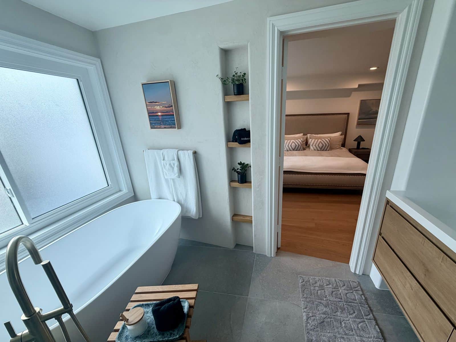 Primary bathroom with a freestanding soaking tub, teak caddy and a small sunset painting