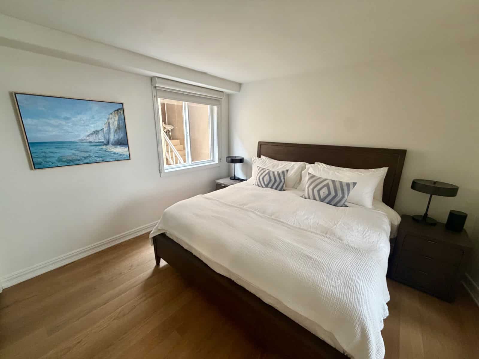 Second bedroom with a dark wood king bed and a large painting of turquoise sea and white cliffs