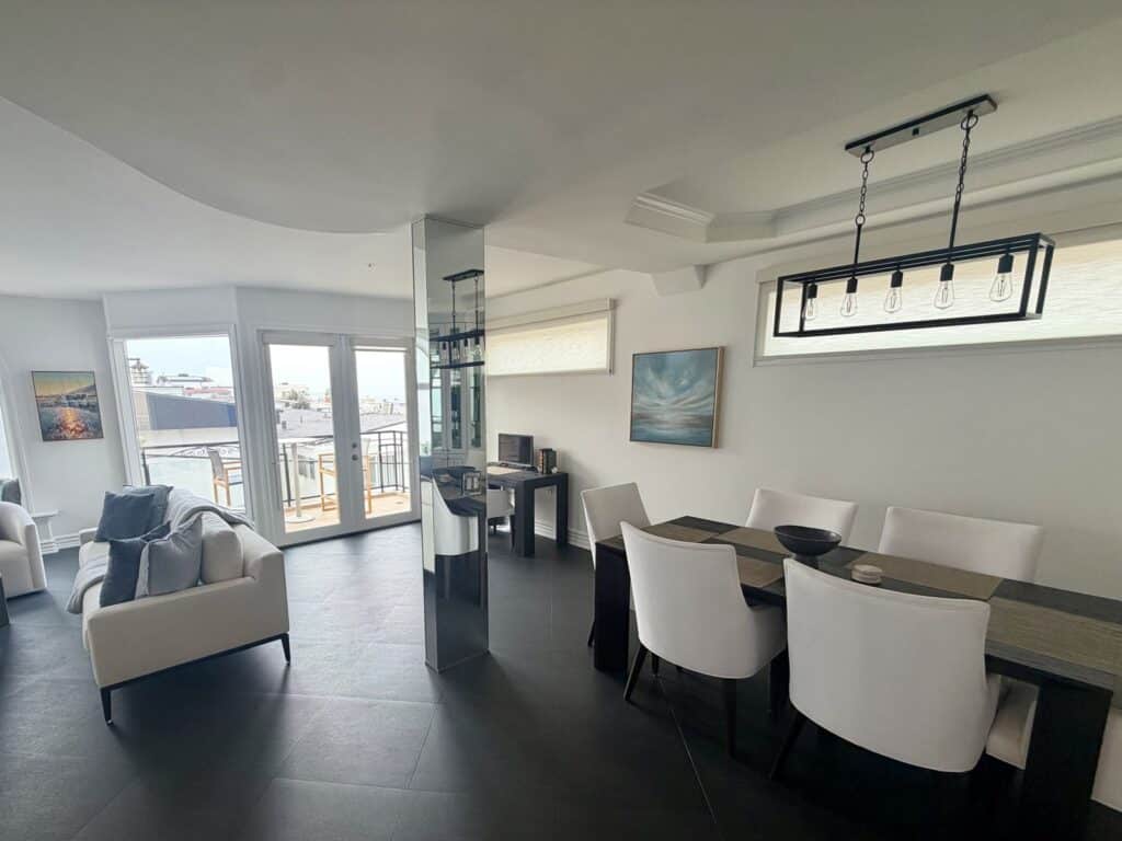 Top floor living and dining space with balcony doors, dining for six and an atmospheric coastal painting