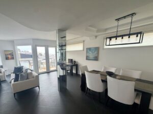 Top floor living and dining space with balcony doors, dining for six and an atmospheric coastal painting