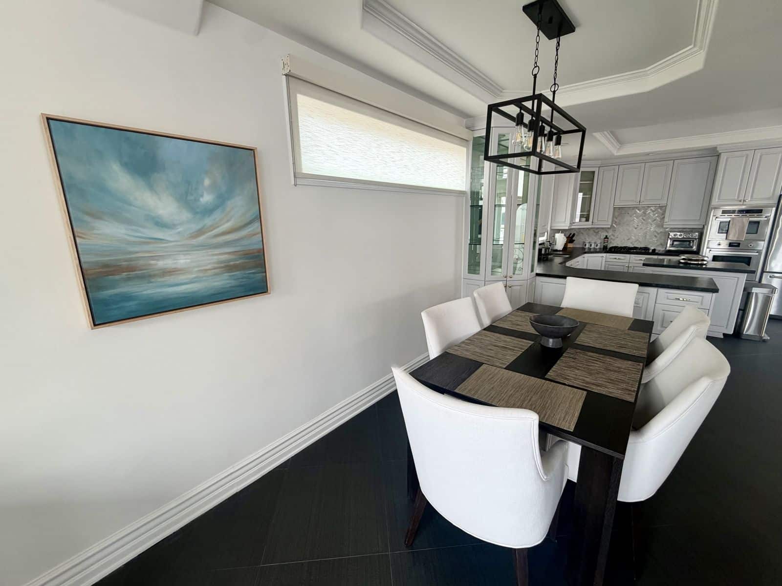 Dining table for six with the chef kitchen behind it and a large sea and sky painting
