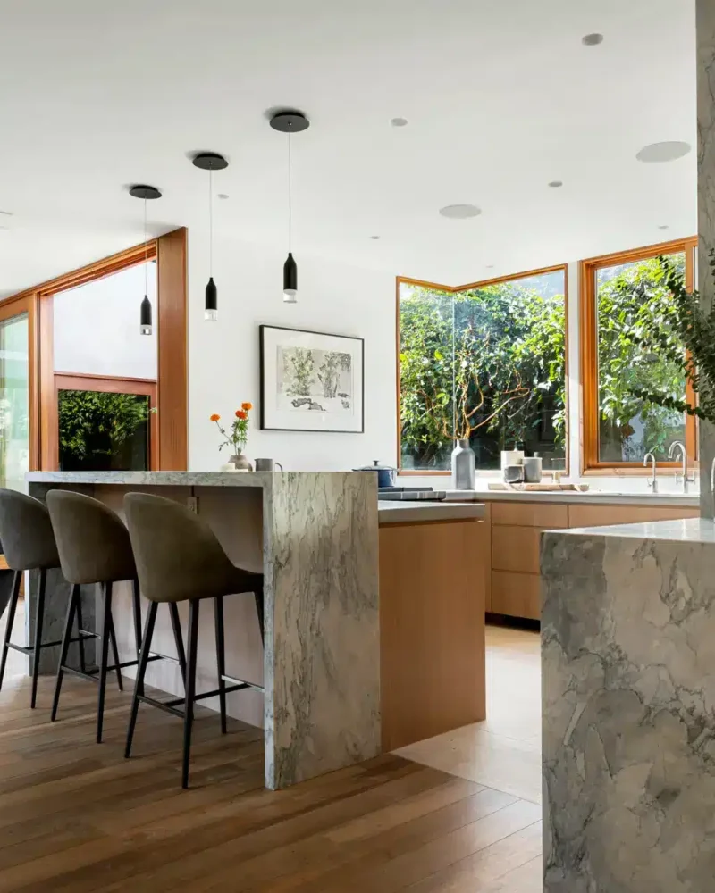 Modern kitchen with marble countertop, wooden cabinets, and bar stools - Open Air Homes