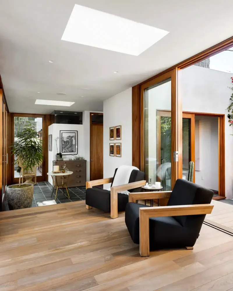 Modern indoor-outdoor living space with wooden flooring, large windows, and seating area - Open Air Homes
