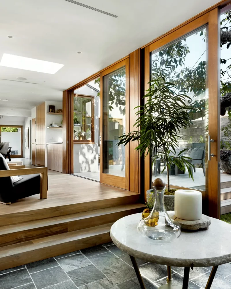 Modern interior with wooden steps, large windows, and tree view - Open Air Homes